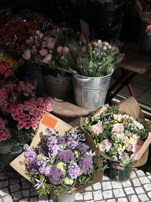 A display of fresh floral bouquets arranged on a rustic wooden table outdoors, featuring a variety of flowers including light pink roses and purple lavender in brown paper wrapping, with additional bo